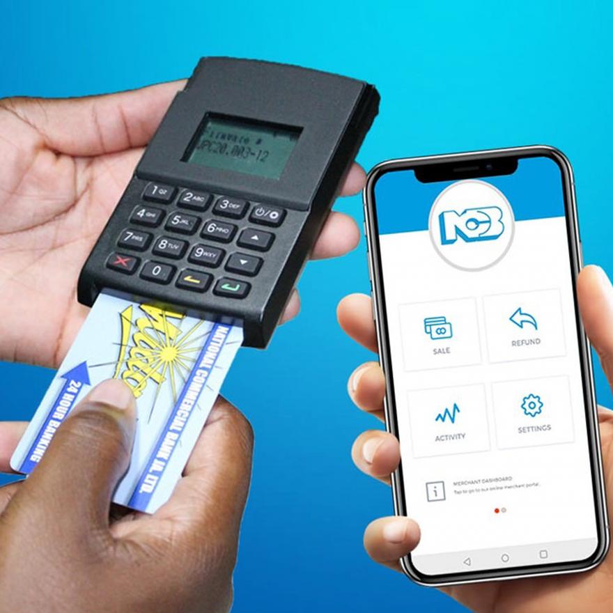 Hand holding a payment card next to a phone and a card reader